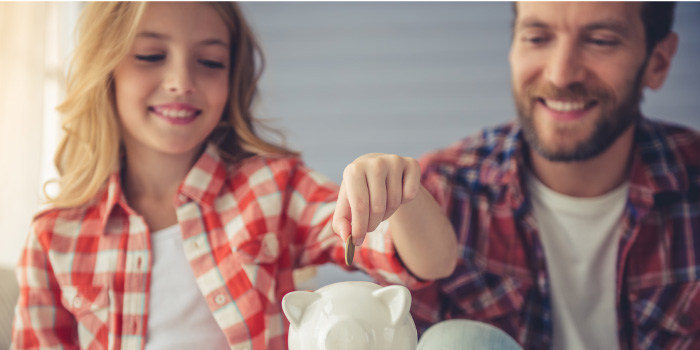 Father helping young daughter put coins in piggy bank