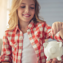 Father helping young daughter put coins in piggy bank