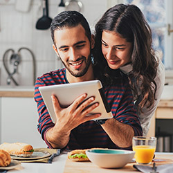 A couple uses a tablet in their kitchen to research homes for sale.